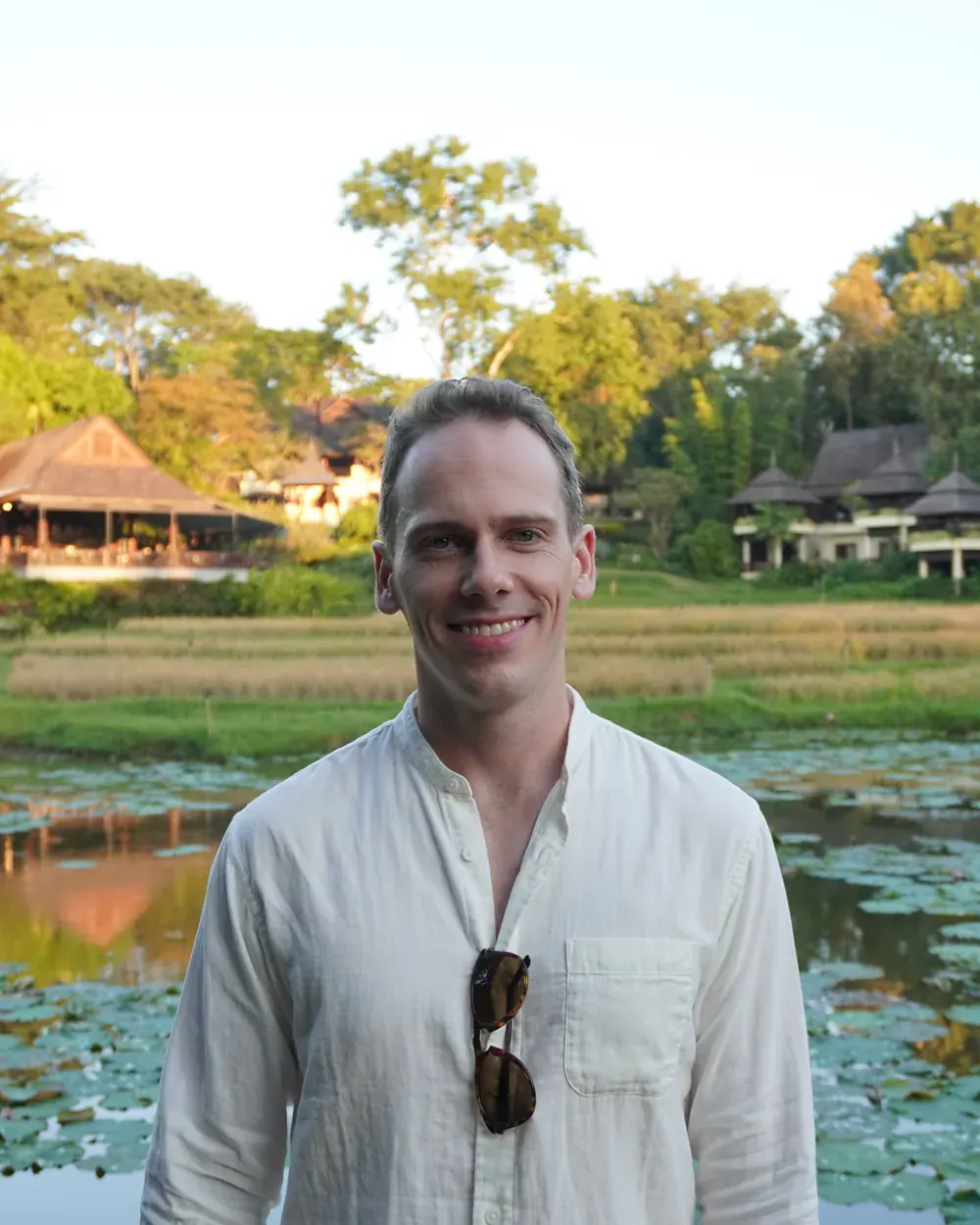 Ambroise Debret en chemise de lin, souriant, devant un étang et des rizières près de Chiang Mai