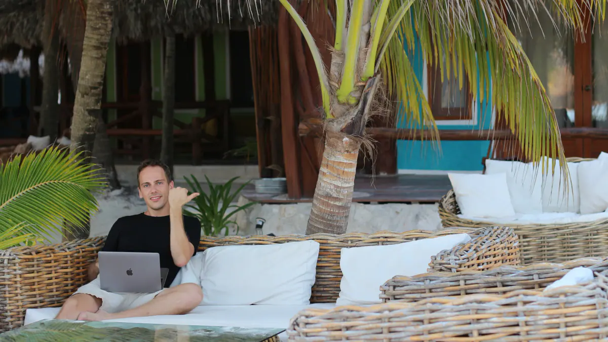 Ambroise Debret au laptop dans un salon en osier sous les palmiers à Holbox