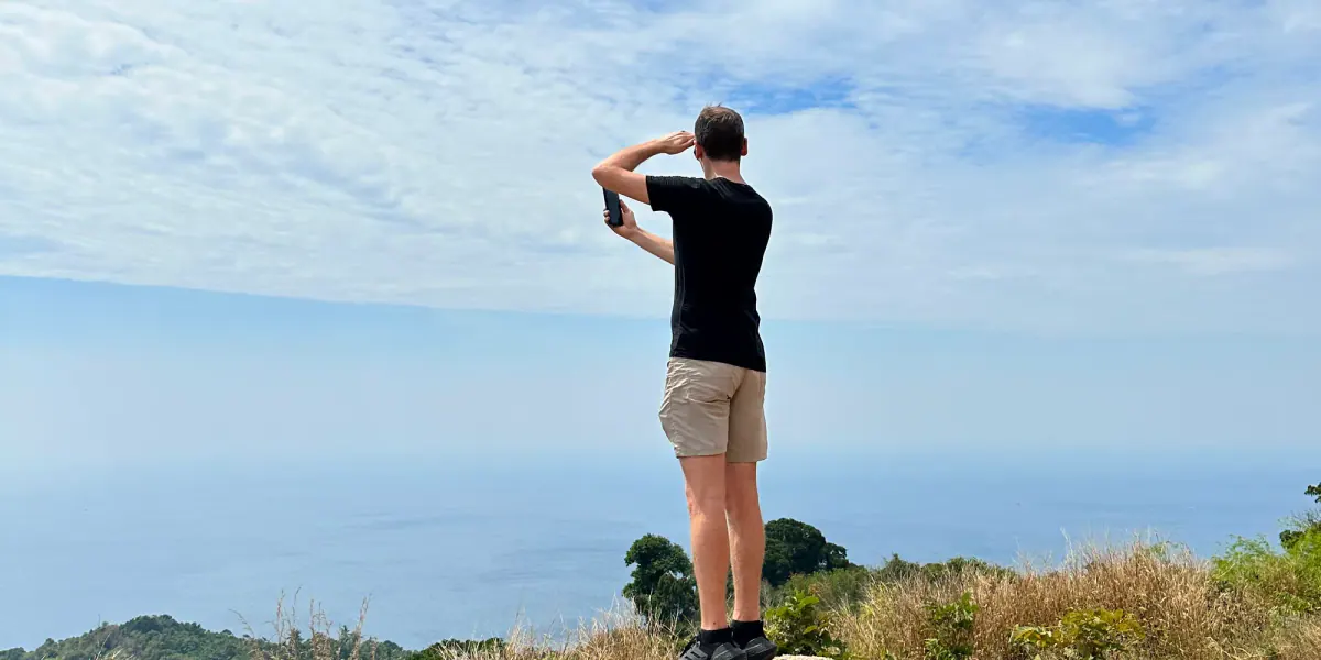 Ambroise Debret de dos sur un rocher, la main en visière face à la mer, à Nai Harn en Thaïlande