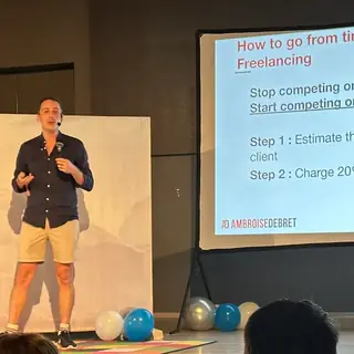 Ambroise Debret sur scène au Bansko Nomad Fest, à côté d’une slide sur la tarification à la valeur en freelance