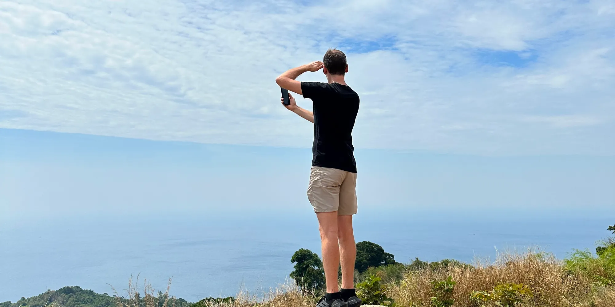 Ambroise Debret de dos sur un rocher, la main en visière face à la mer, à Nai Harn en Thaïlande