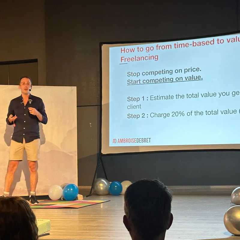 Ambroise Debret en conférence au Bansko Nomad Fest, à côté d'une slide sur la tarification à la valeur en freelance