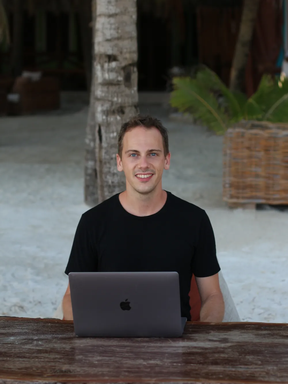 Ambroise Debret souriant derrière son laptop, sur une table posée dans le sable à Holbox